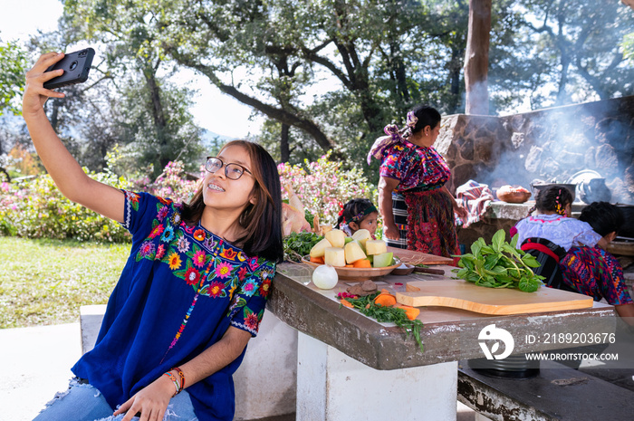 Chica haciendose una selfie con el telefono celular. Familia cocinando en una estufa de leña al aire