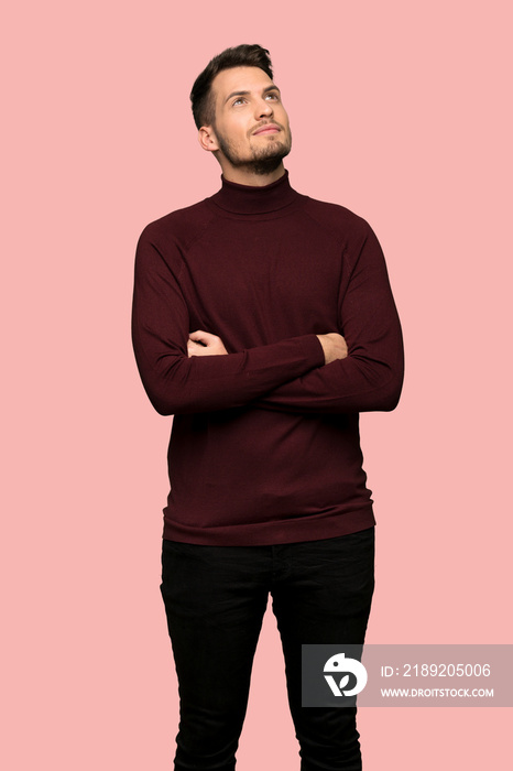 Man with turtleneck sweater looking up while smiling over pink background