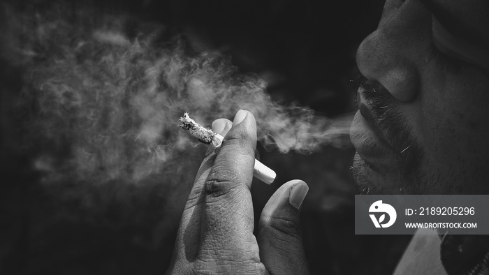 Focus at hand of Asian man is smoking cigarette in dark tone with black and white style