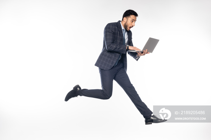 shocked businessman in suit jumping while using laptop on white.