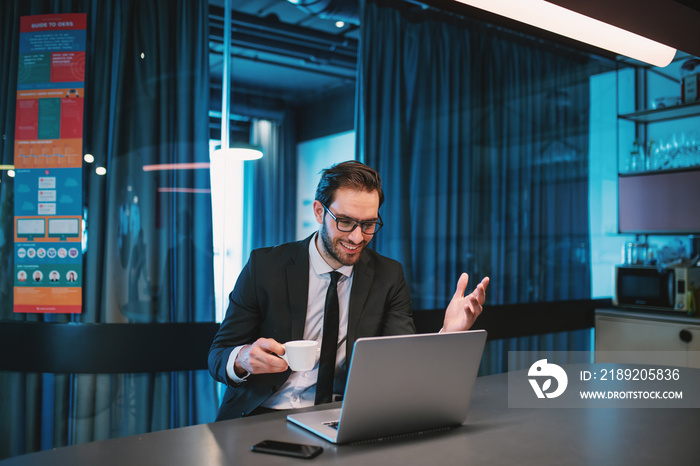 Attractive optimistic caucasian bearded businessman in suit and with eyeglasses sitting in company k