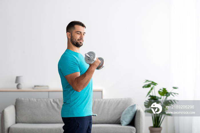 Concentrated serious millennial european guy doing strength exercises for arms and lifting dumbbells