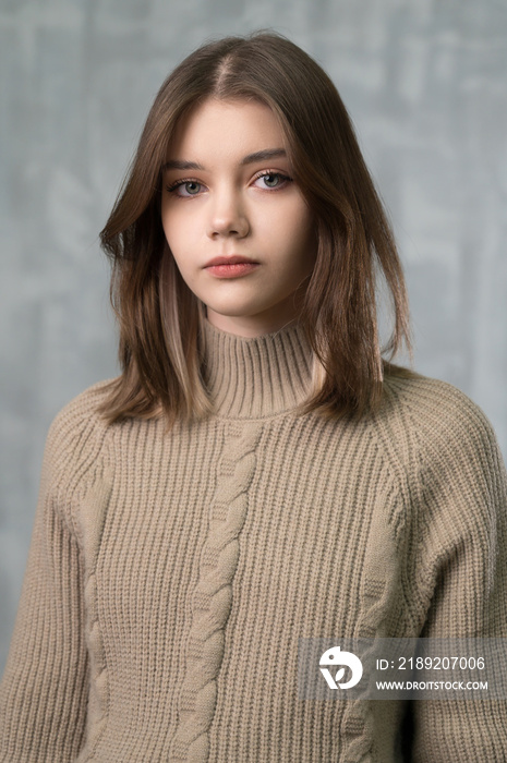 娃娃脸的年轻漂亮女孩的工作室肖像。背景是灰色墙壁。针织毛衣。