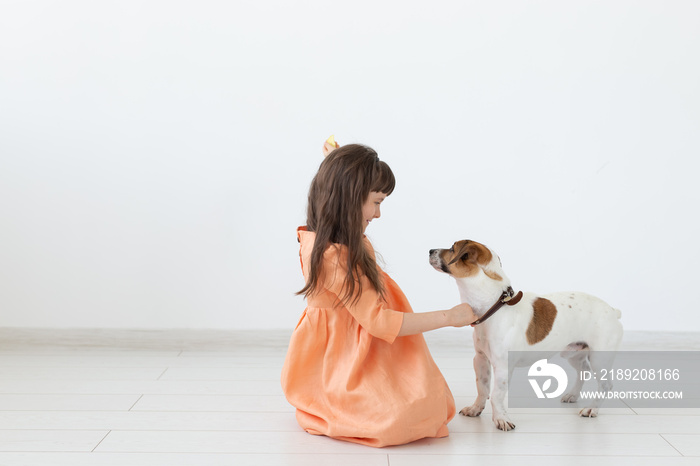 Little girl with dark hair plays with her beloved dog while sitting on the floor in a peach dress ag