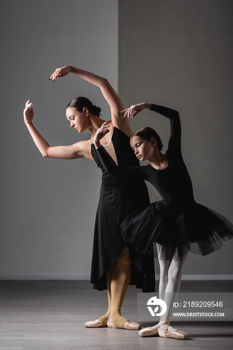 full length view of girl in black tutu training near graceful ballet teacher