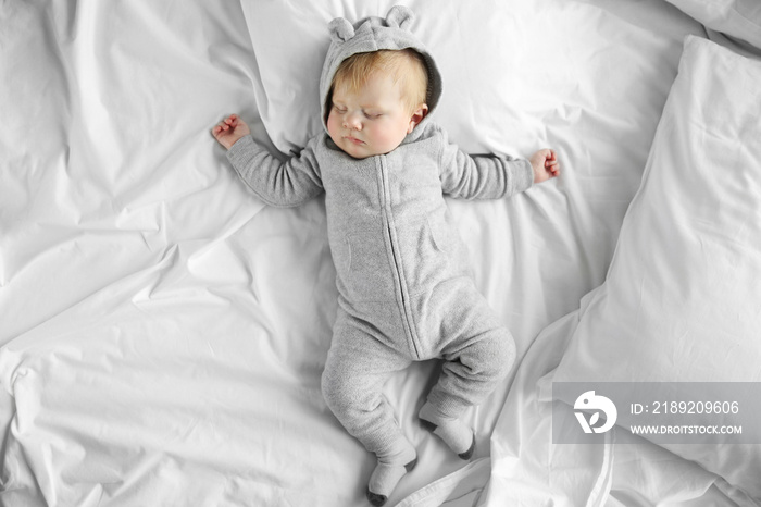 Little baby boy in grey pajamas sleeping on the bed