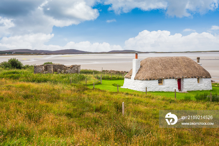 Traditionally built white cottage with thatched roof, next to the turquoise bay, with stormy cloudy 