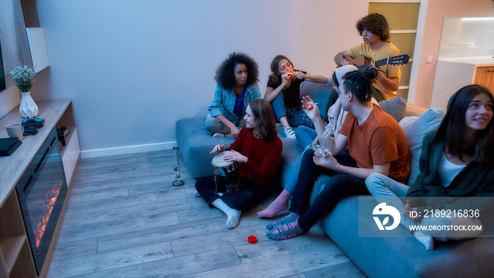 Young multicultural people smoking weed, marijuana together, playing music and relaxing on the sofa 