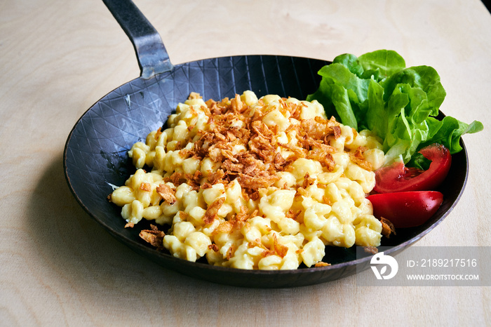 Bayrische Käsepätzle Kasspatzen mit Röstzwiebeln in einer Eisenpfanne auf einem Holztisch