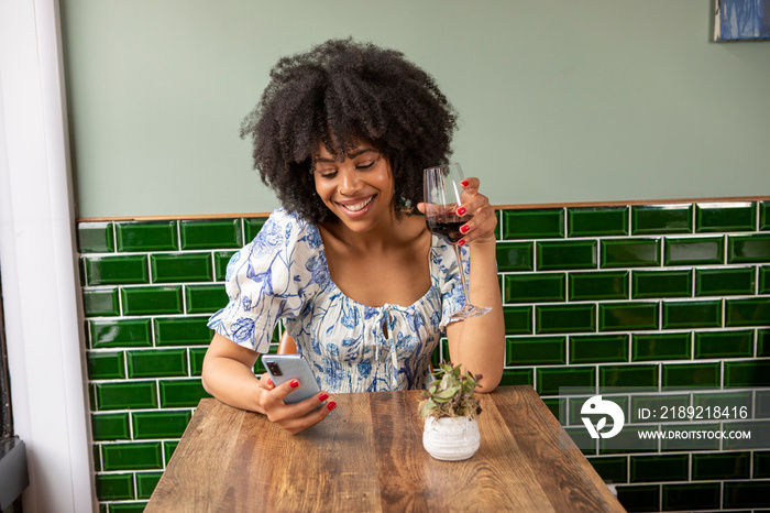 UK, London, Smiling woman with glass of red wine and smart phone at cafe table