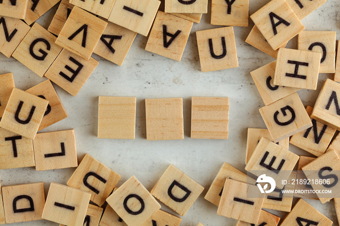 Top down view, pile of square wooden blocks with letters on white board. Three empty tiles for your 