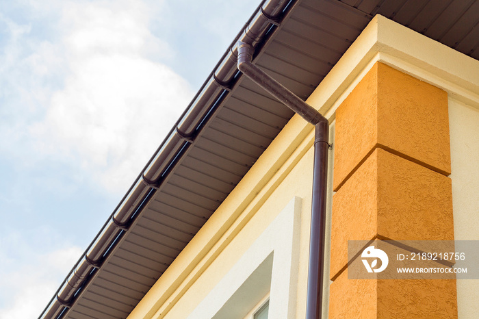 Close-up detail of cottage house corner with brown metal planks siding and roof with steel gutter ra