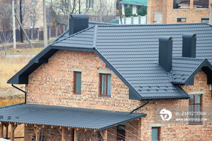 Chimney on house roof top covered with metallic shingles under construction. Tiled covering of build