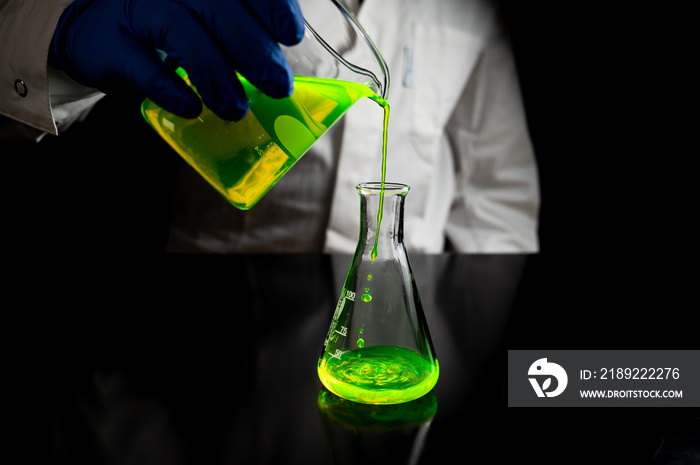 A research scientist experimenting with a green fluorescent droplets in a glass conical flask in dar