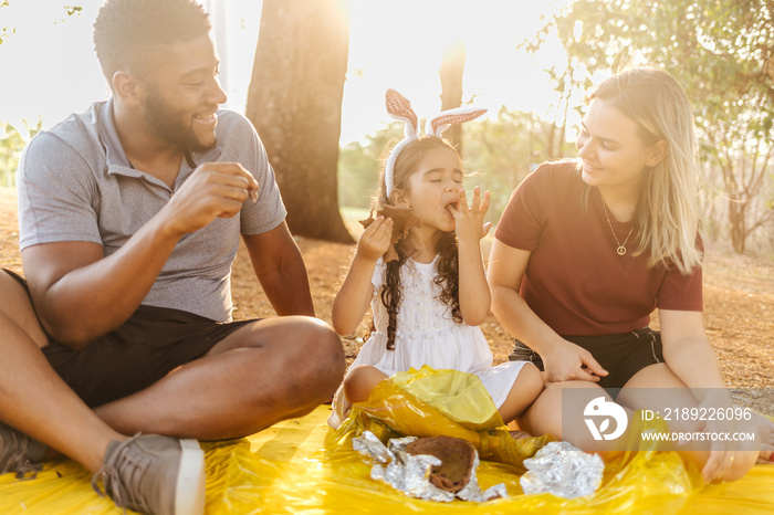 Latin family celebrating Easter. Curly girl wearing bunny ears and eating delicious chocolate egg