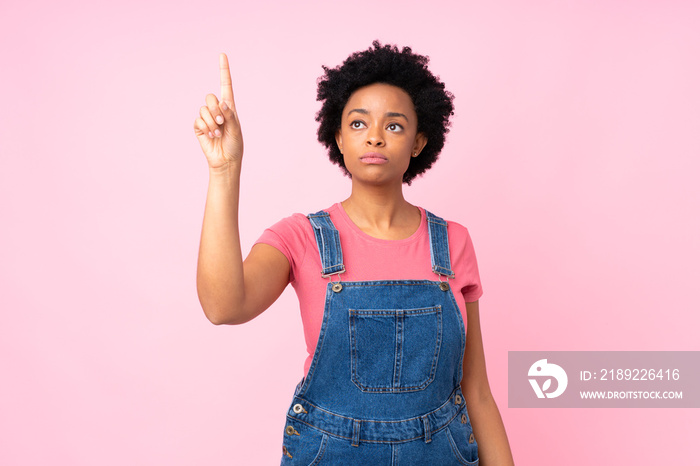 African american woman with overalls over isolated pink background touching on transparent screen