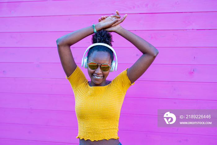 black woman dancing smiling, pink background in contrast with yellow clothes and jeans, afro fashion