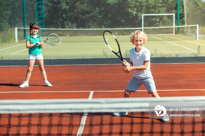 Brother and sister feeling joyful while playing tennis outside