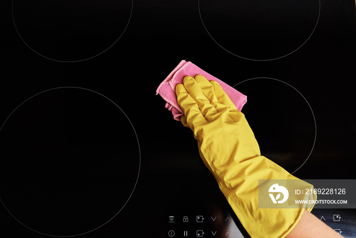 Cleaning induction stove. Woman in yellow rubber gloves cleans kitchen induction hob with cleaning s