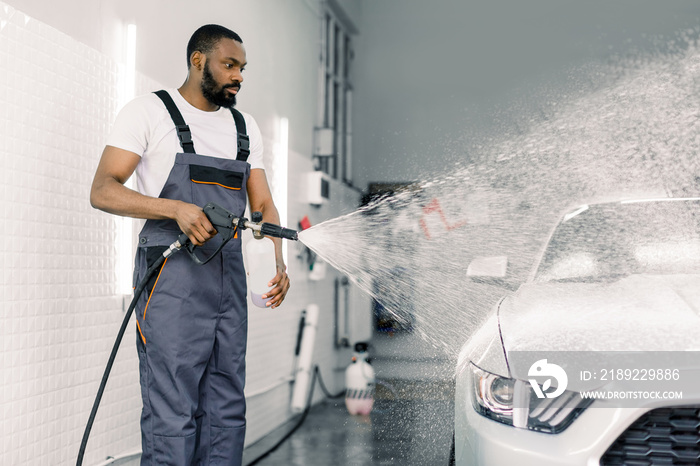 African American man, car wash worker is spraying cleaning foam to a modern white luxury car holding