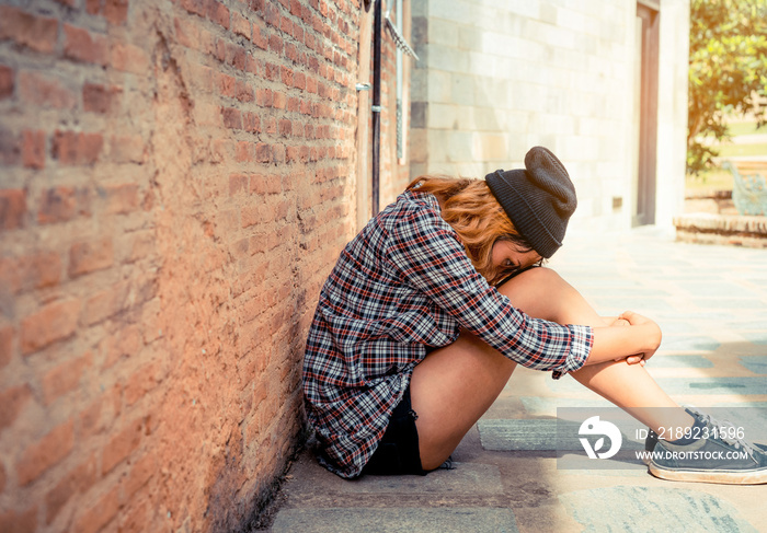 Depressed teenage woman feeling sad alone against brick wall in old town. Education and family failu