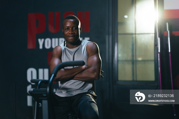 African ethnicity man listening music while using spinning bike on cardio machine in fitness gym