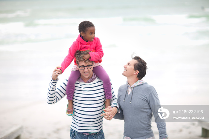 Gay couple walking on beach with child on shoulders