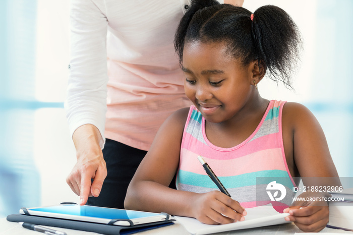 白人老师帮助黑人小女孩在平板电脑上做作业。