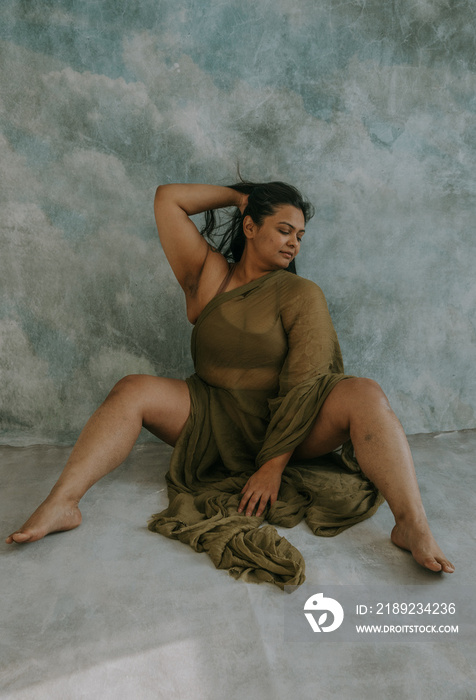 East Indian woman sitting on floor with one hand in hair, the other on the floor looking down