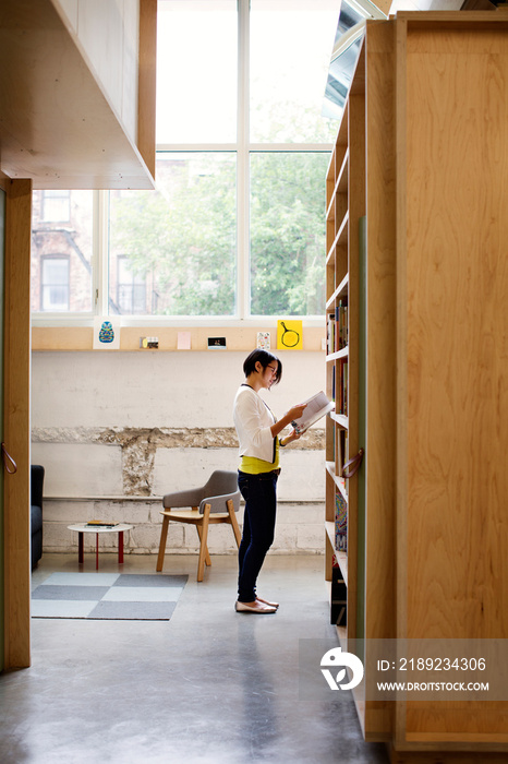 Young woman reading book in front of book shelf in library