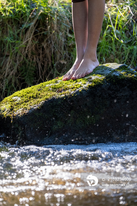 站在溪流苔藓覆盖的岩石上的女人的赤脚