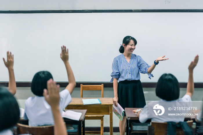 一位面带微笑的亚洲女高中老师在教室里用a教着穿白色制服的学生