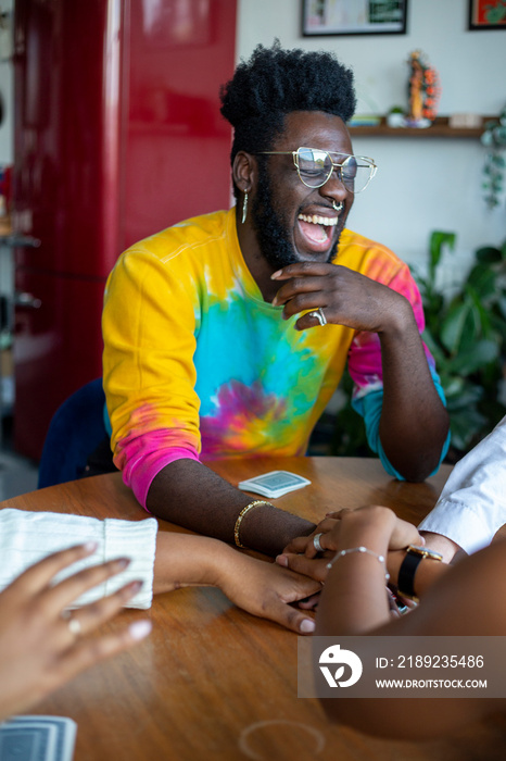 Man laughing while holding hands with friends at table�