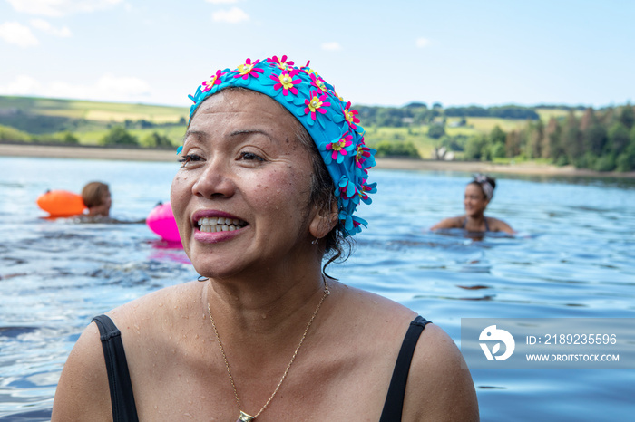 Smiling woman in floral swimming cap in lake, Yorkshire, UK