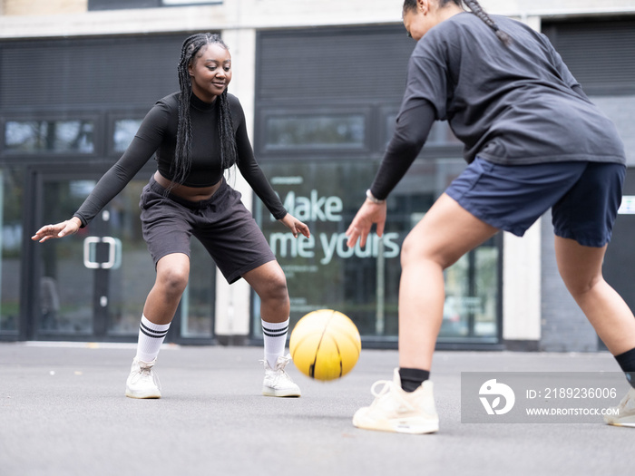 Two female friends playing basketball outdoors