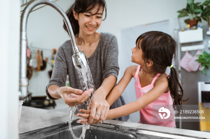 mother and daughter wash their hand together in the kitchen sink