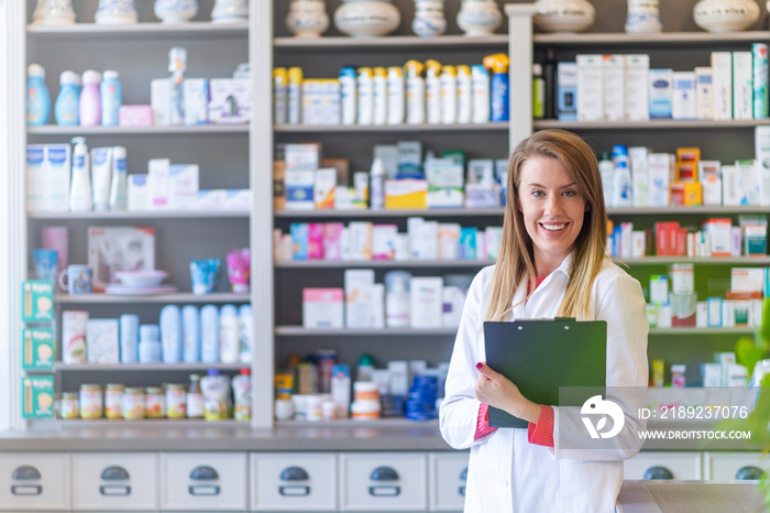 Young female pharmacist at work. Blurred shelves with pharmaceutical products on background. Pharmac