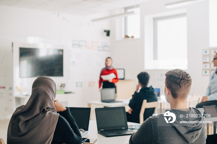 Classmate looking at female student giving presentation in classroom