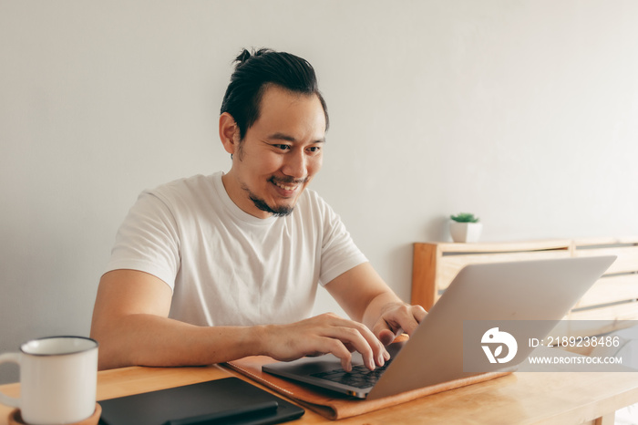 Happy Asian man is working with laptop in his apartment bedroom in concept of Work From Home and Wor