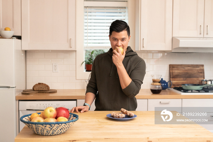 亚裔美国人在厨房里拿着一个苹果。