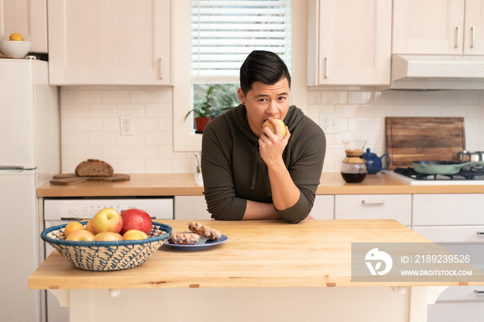 亚裔美国人在厨房里拿着一个苹果。