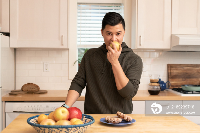 Asian American man with an apple in the kitchen.