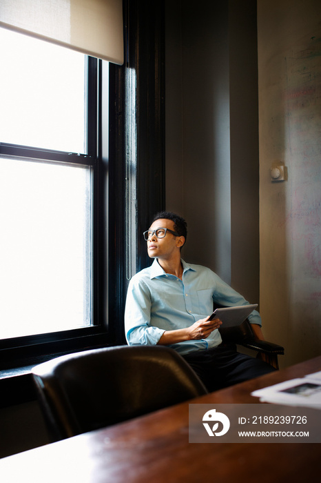 Thoughtful businessman with digital tablet looking through window