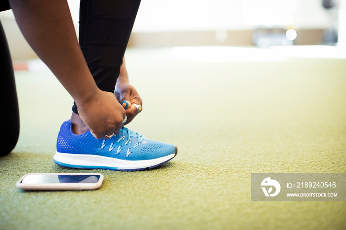 Low section of female athlete tying shoelace on carpet in gym