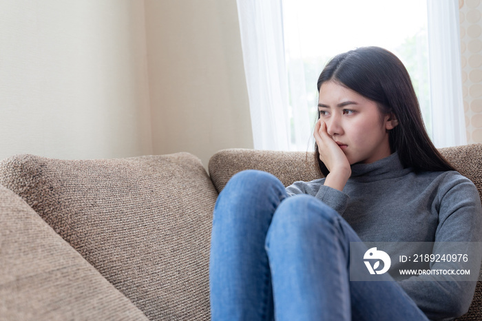 一个闷闷不乐的亚洲漂亮年轻女子独自坐在沙发上，情绪激动的特写脸