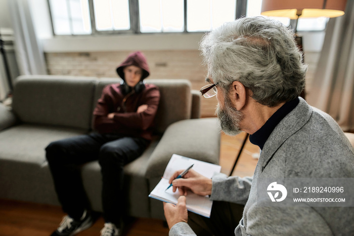 Psychoanalyst taking notes during appointment with uneasy teenage boy