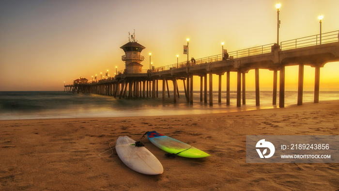 pier at sunset with surfboards in the sand