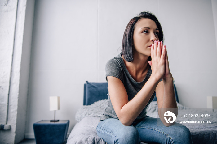 beautiful depressed woman sitting on bed and covering mouth at home