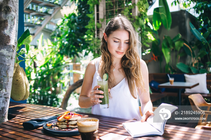 Relaxed female reading book and sipping vitamin beverage in bar