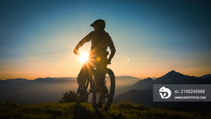 Silhouette of a woman on mountain bike looking at sunset